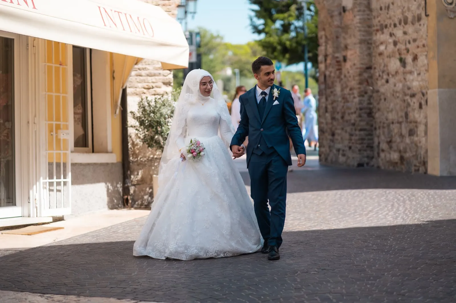Gli sposi passeggiano mano nella mano lungo una via pedonale del borgo di Lazise, accanto alle mura di pietra