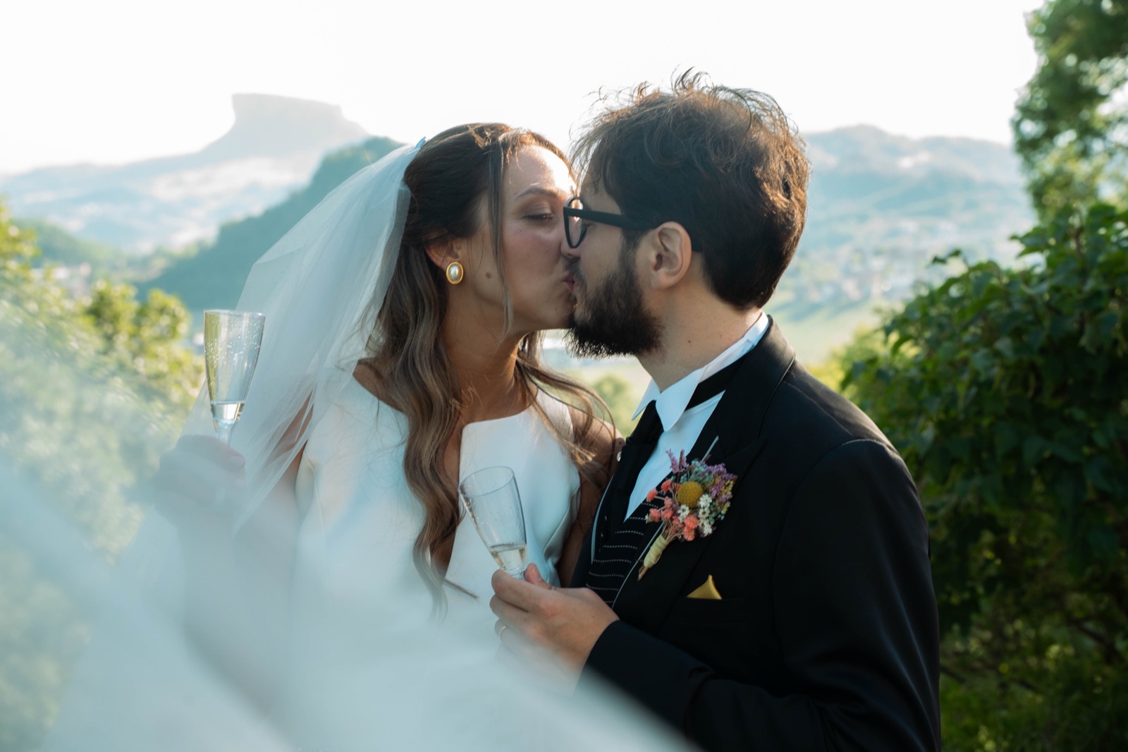 Gli sposi si baciano al tramonto sulle colline emiliane, calici in mano