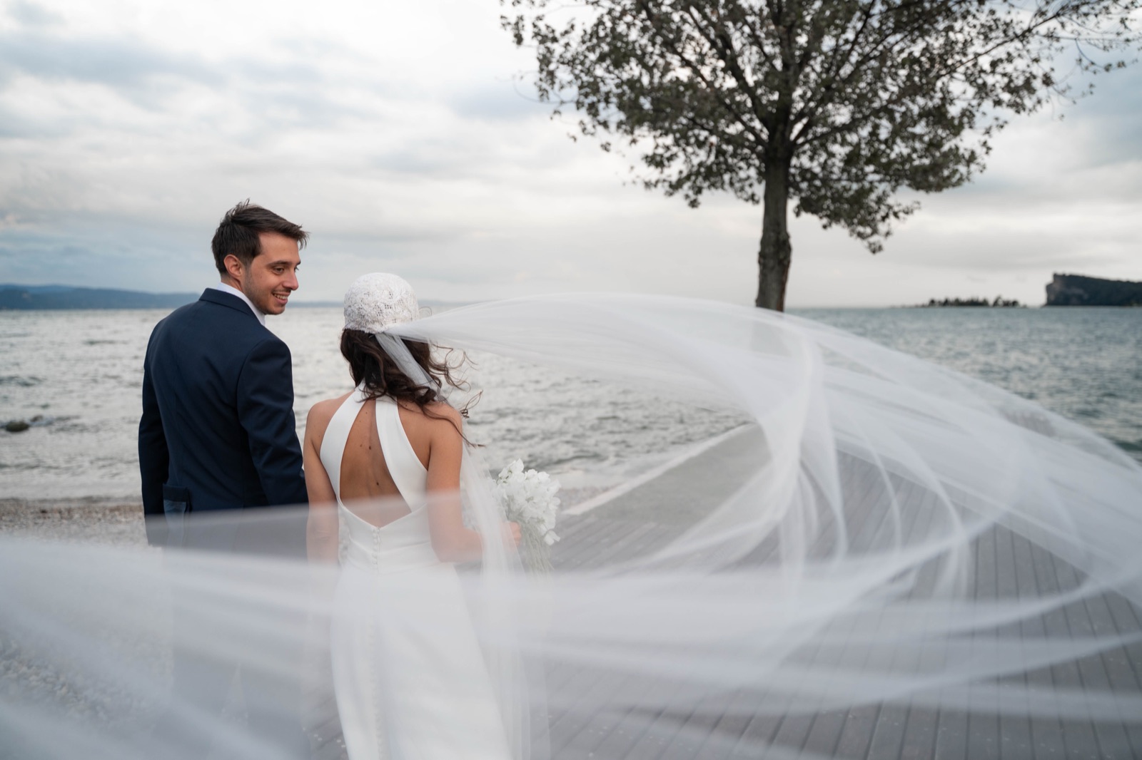 Gli sposi in riva al lago, con il velo che vola nel vento